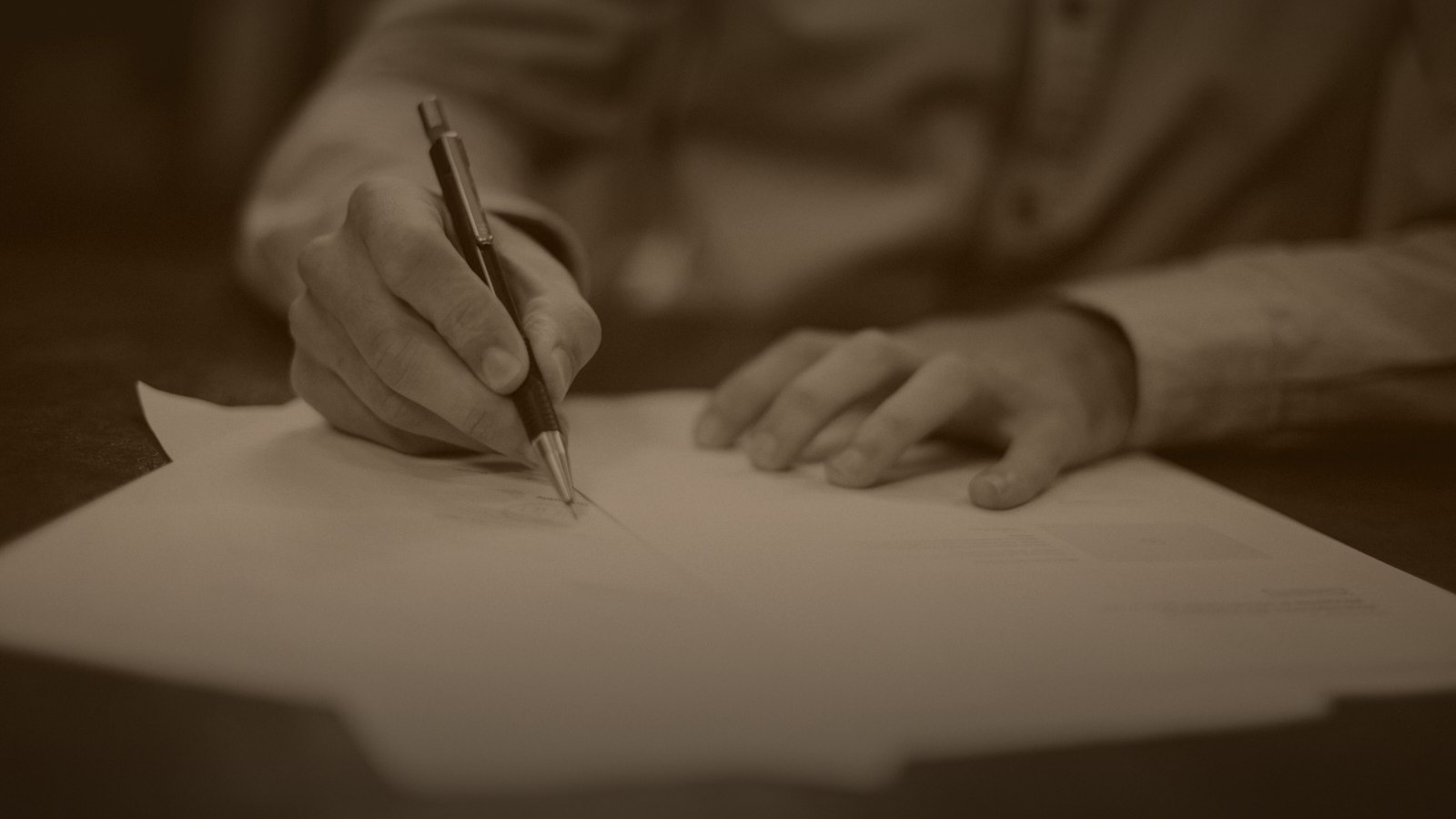 Sepia-toned photo of a hand reviewing documents with a pen