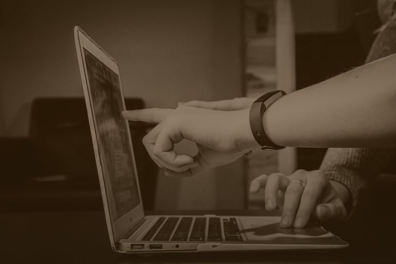 Sepia photo of hands pointing at a laptop screen, representing buyer questions asked in the AI apps