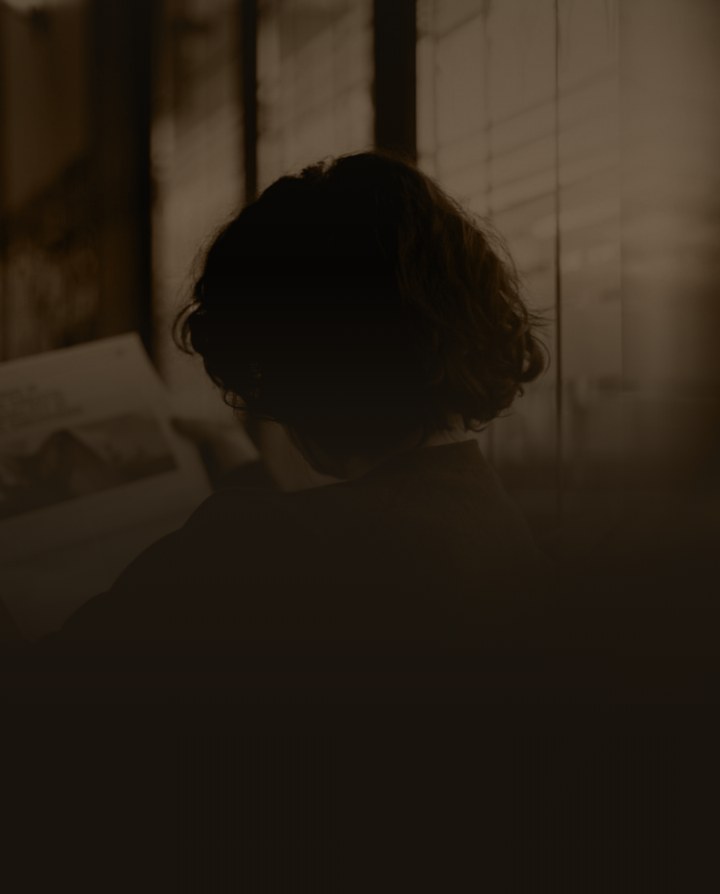 A person reading printed pages by a window, in MentionShare's sepia tone